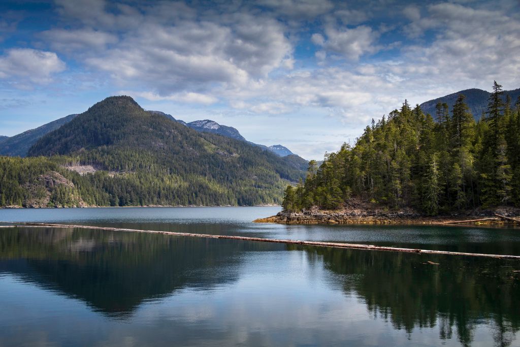 A calm bay with mountains in the background and a few clouds in the sky