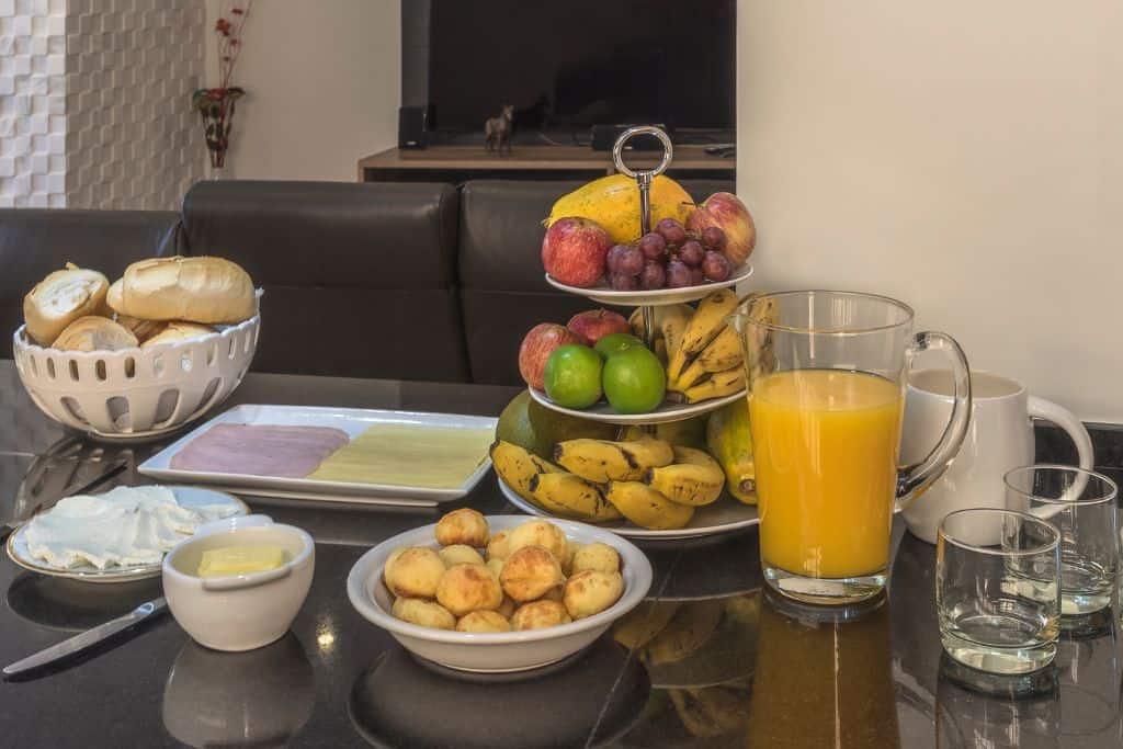 A traditional brazilian breakfast spread, including bread, ham and cheese, cheese bread, fruit and orange juice
