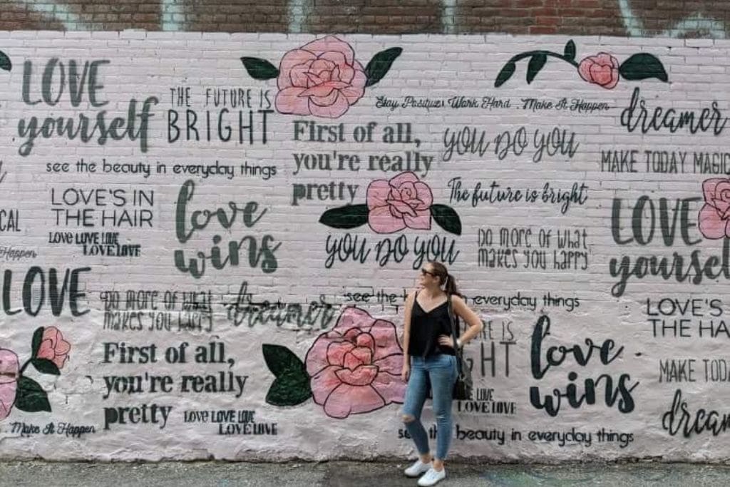 A woman standing in front of a pink mural depicting love quotes in Graffiti Alley in Toronto