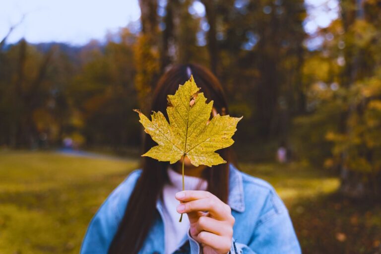 Immigration consultant vs lawyer: A woman holding a yellow maple leaf in front of her face.