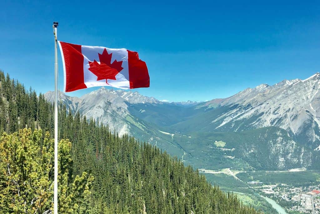 A Canadian flag flying in the wind with a mountain landscape in the background.