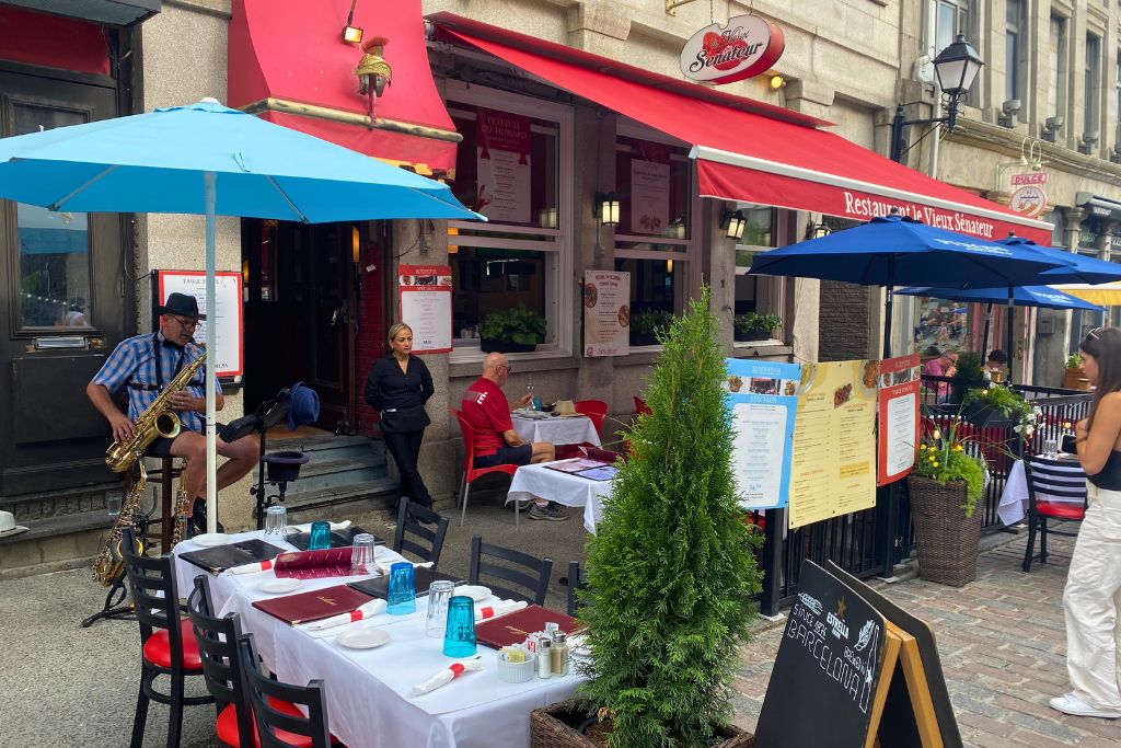 A man playing a saxaphone on the sidewalk patio of a restaurant in Old Montreal.