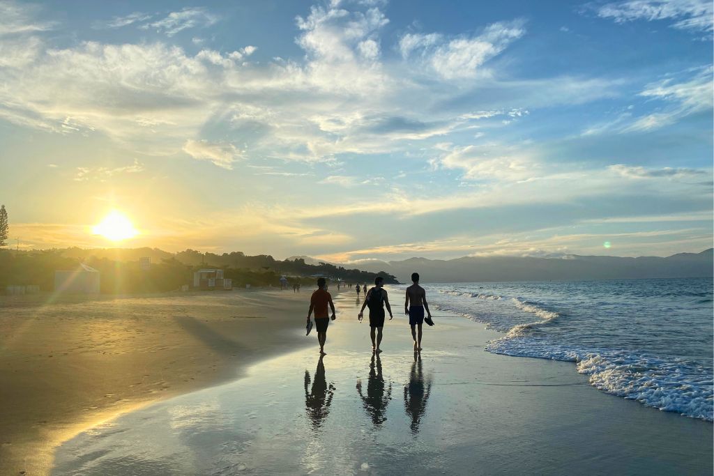 Three men walking along a beach at sunset in Florianopolis, Brazil