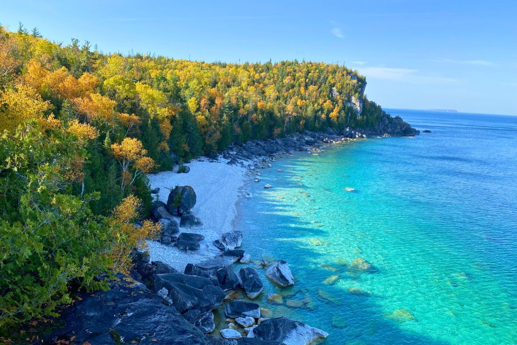 A white pebble beach and turquoise blue water during fall in Georgian Bay, Ontario.