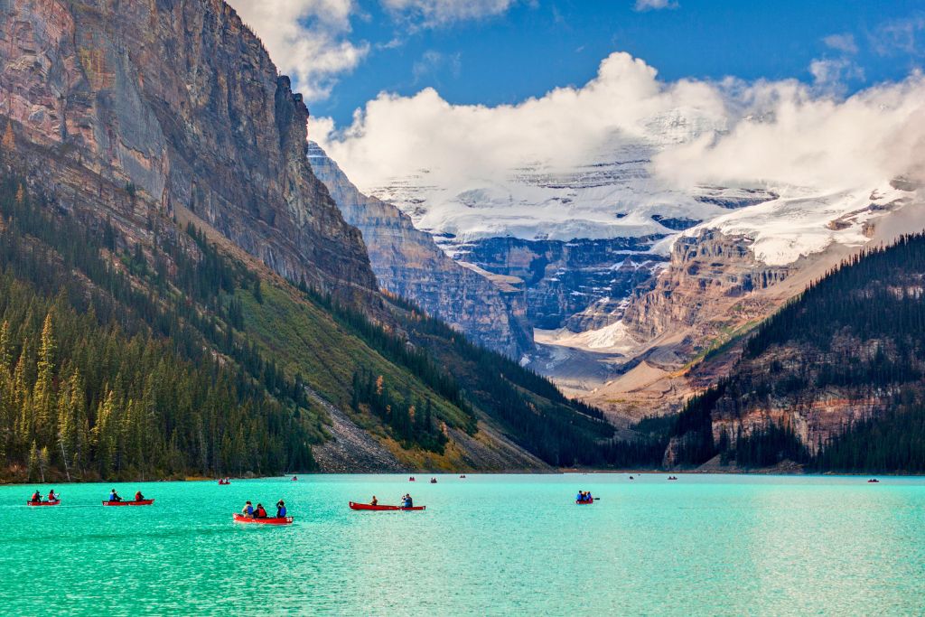 Several tourists canoeing in Canada on Lake Louise's bright turquoise water.