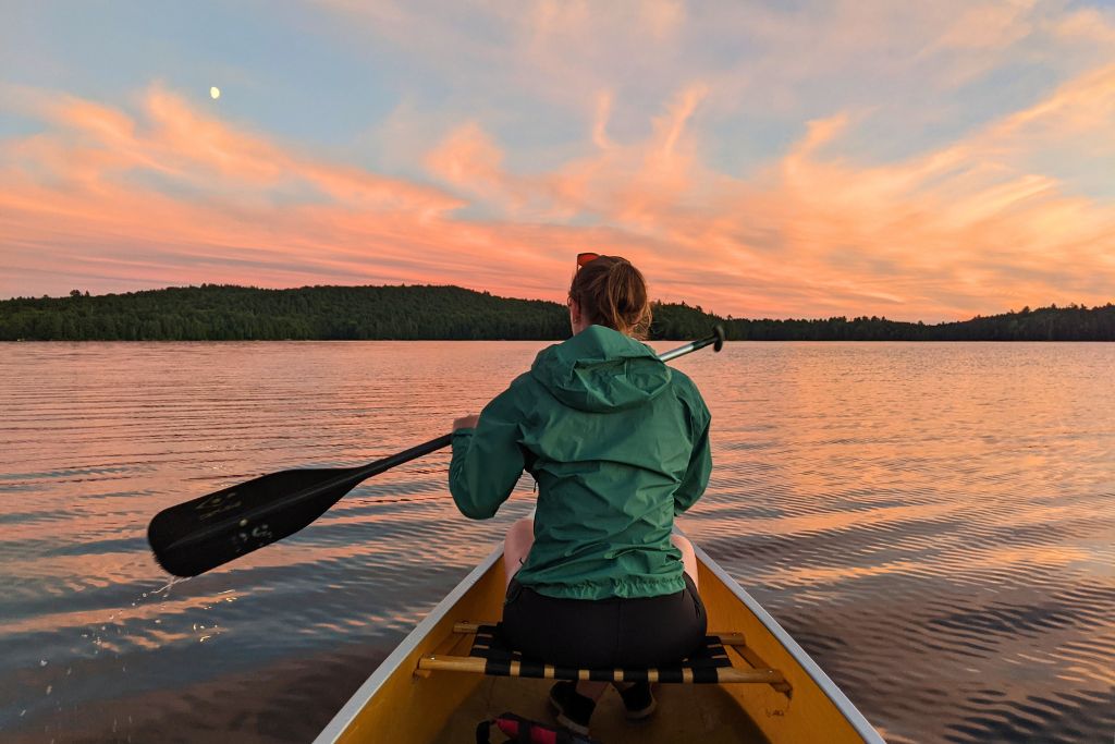 A woman canoeing in Canada at sunset, on a lake in Algonquin Provincial Park.