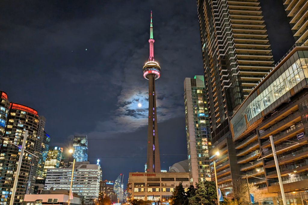 A view of the CN Tower in Toronto at night, with the moon shining through the clouds.
