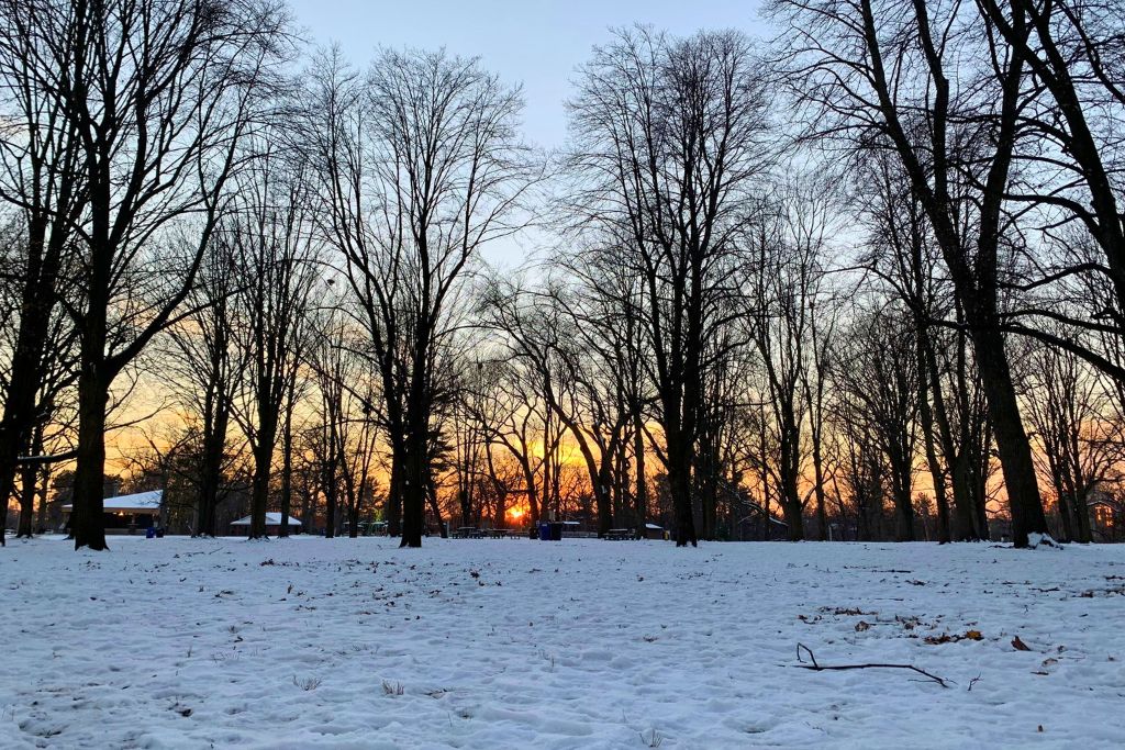 A snow covered park in Toronto with the sun setting in the late-afternoon in the background. These shorter days in winter are one of the cons of living in Canada.