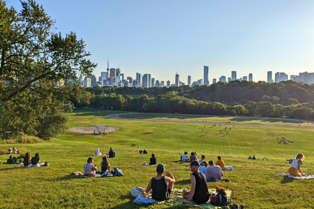 People relaxing on the grass and watching the Toronto skyline at Riverdale Park.