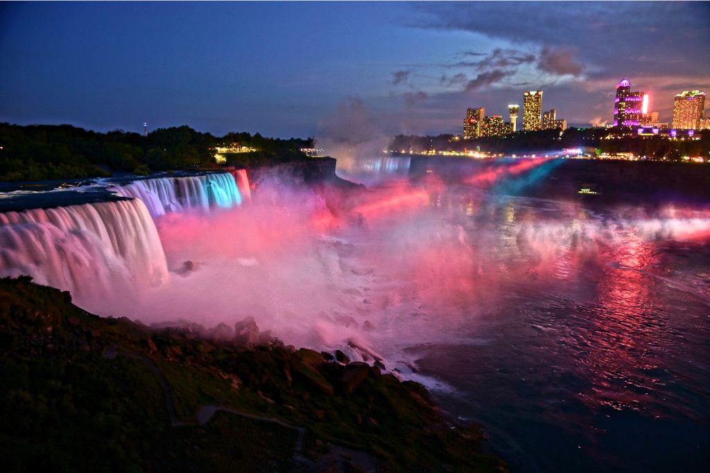 The view of Niagara Falls lit up at night with red and blue lights.
