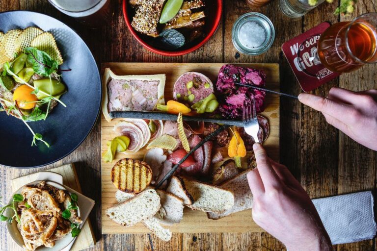 A charcuterie board on an apéritif table, with someone's hands visible as they cut into some pate.