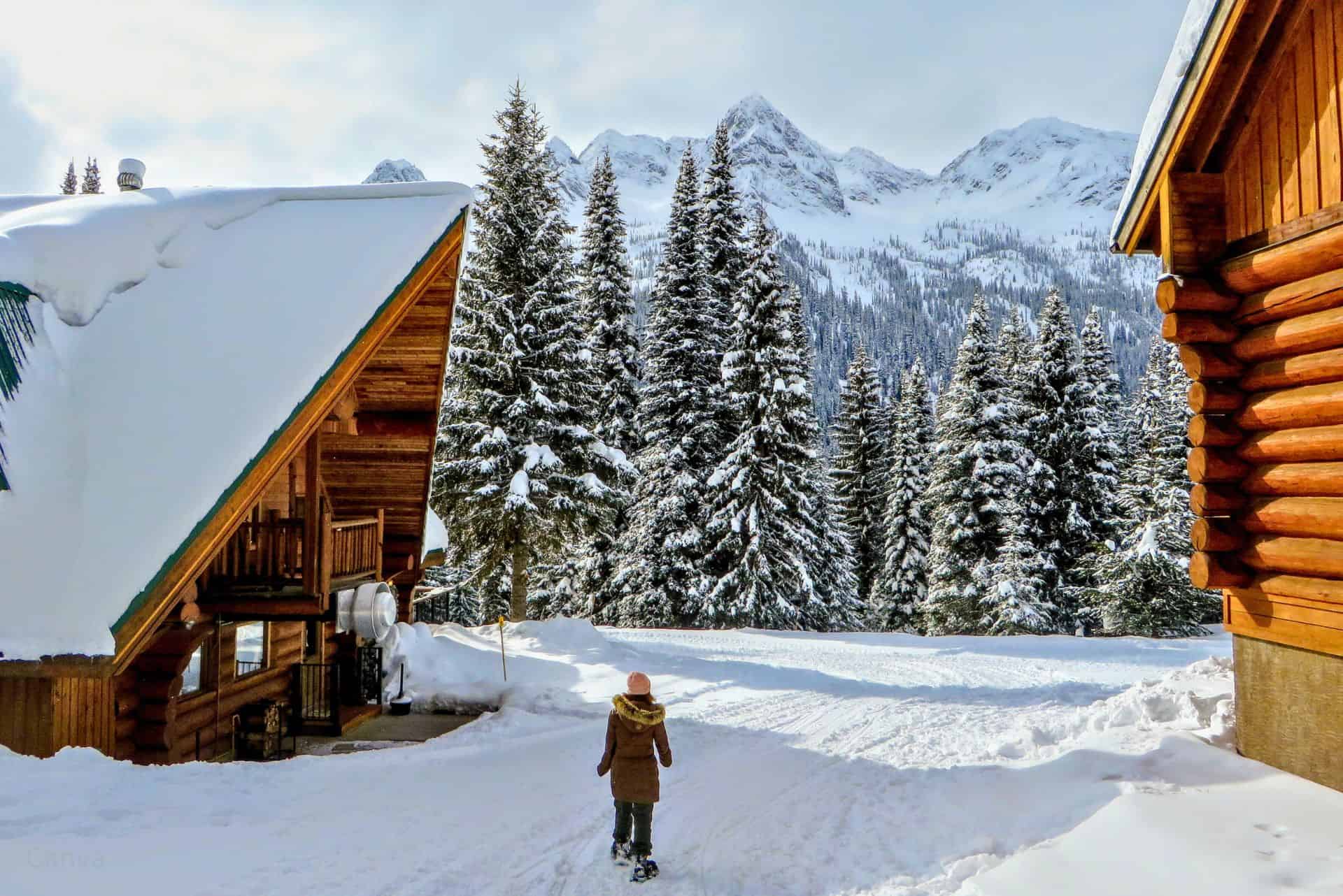 A young female snowshoer walking in between two wood cabins during the winter in the remote snow covered forests of Fernie, British Columbia, Canada. Photo by Chris Babcock via Canva.com.